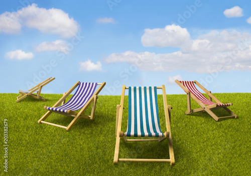 Four wooden beach striped chaise-longues standing on green grass under blue summer sky. Summer and travel composition.