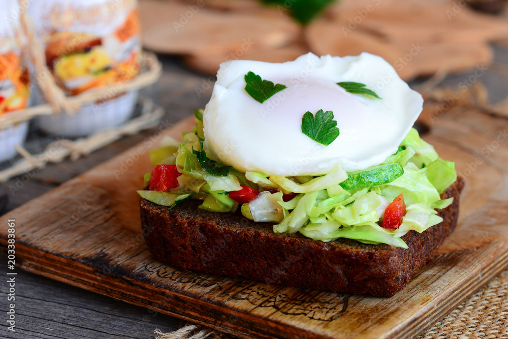 Poached egg toast sandwich. A poached egg on a rye bread slice with coleslaw, cucumber, red pepper and fresh parsley. Quick and easy healthy food. Wooden background. Rustic style. Closeup Poached egg toast sandwich. A poached egg on a rye bread slice with coleslaw, cucumber, red pepper and fresh parsley. Quick and easy healthy food. Wooden background. Rustic style. Closeup