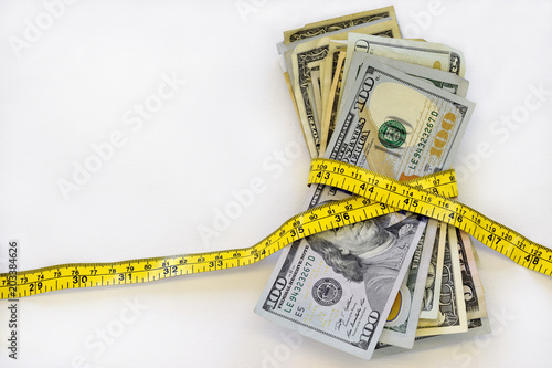 Stack of cash, US dollars, with measuring tape, against white background.