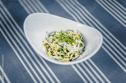 Top view of a salad in the white plate on the table with a blue tablecloth in white strips. photo