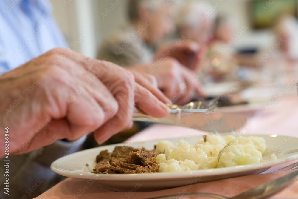 Elderly care home. Diner. Elderly man eating his plate with potatoes and meat. Fork and knife. Having dinner in a elderly home.