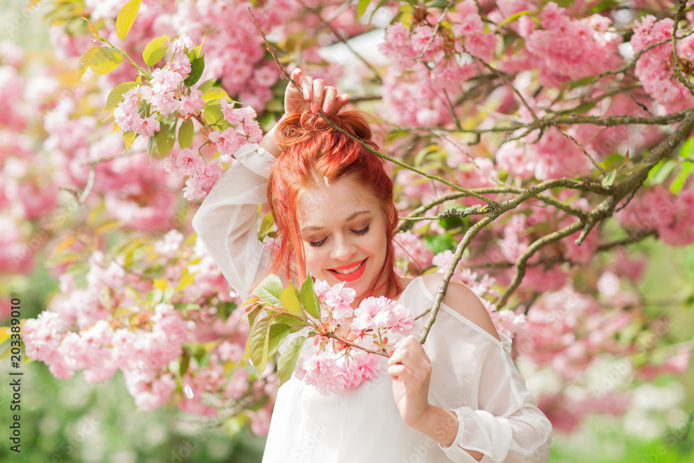 Beautiful young woman with red hair having fun standing in cherry blossom tree, springtime garden mood Beautiful young woman with red hair having fun standing in cherry blossom tree, springtime garden mood