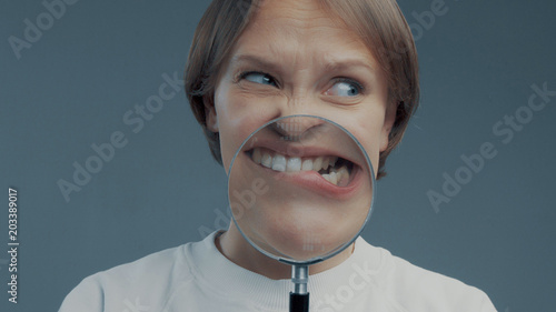 portrait of caucasian wooman with magnifier makes fun faces. Magnifier to the mouth. Woman nervious bite lips photo