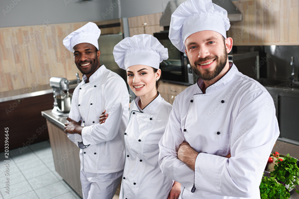 Multiracial team of cooks looking at camera by cooking table