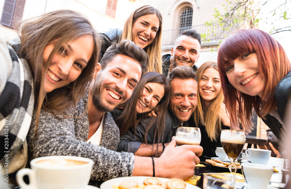Friends taking selfie at bar restaurant drinking cappuccino and irish coffee - People having fun together at fashion cafeteria - Friendship concept with happy men and women at cafe - Warm filter
