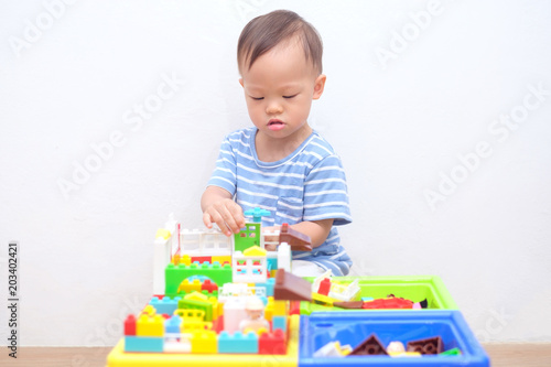 Cute little Asian 18 months / 1 year old toddler boy child sitting on wooden floor having fun playing with colorful building blocks indoor at home, Educational toys for young children concept