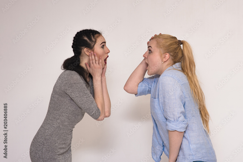Portraits on the gray background of two girls girlfriends showing emotions. Portraits on the gray background of two girls girlfriends showing emotions.
