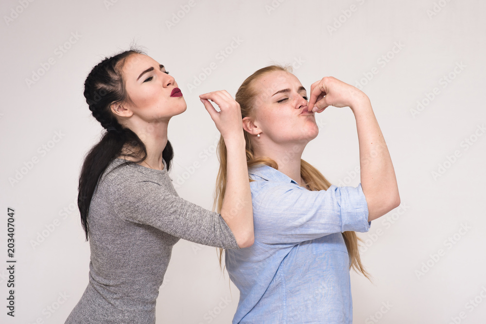Portraits on the gray background of two girls girlfriends showing emotions. Portraits on the gray background of two girls girlfriends showing emotions.