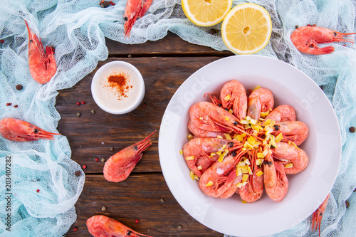 Shrimps boiled with sauce and pieces of a lemon on a dark wooden background