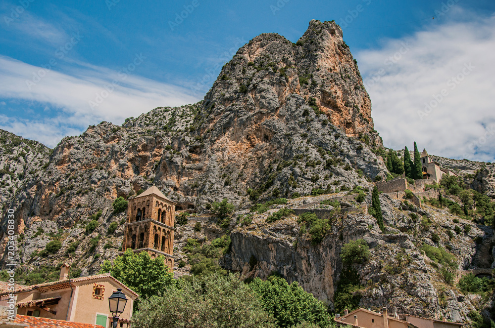 View of the church Notre-Dame de Beauvoir amid the cliffs and houses of the charming village Moustiers-Sainte-Marie. In the Alpes-de-Haute-Provence department, Provence region, southeastern France