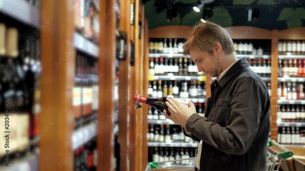 Smiling man holding bottle of wine in supermarket choose champange in shop store Smiling man holding bottle of wine in supermarket choose champange in shop store