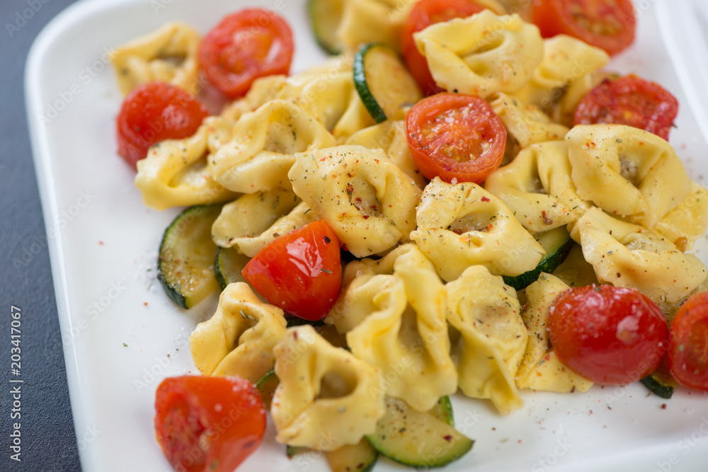 Close-up of tortellini with roasted cherry tomatoes and zucchini slices, selective focus Close-up of tortellini with roasted cherry tomatoes and zucchini slices, selective focus