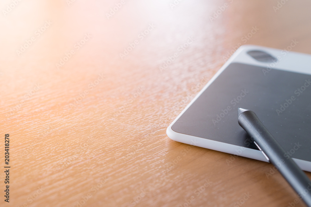 the stylus pen and the pad are on the wooden desk. the stylus pen and the pad are on the wooden desk.