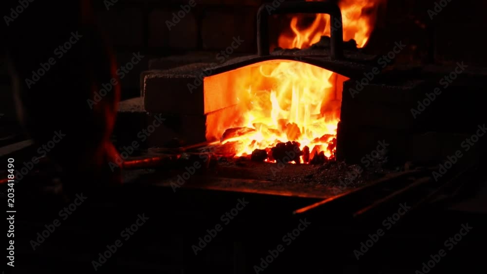 Closeup of a blacksmith fanning the flames of the furnace, using the tools prevents embers, sparks flying to the side in slow motion. Close-up of blacksmith's hand. Closeup of a blacksmith fanning the flames of the furnace, using the tools prevents embers, sparks flying to the side in slow motion. Close-up of blacksmith's hand.
