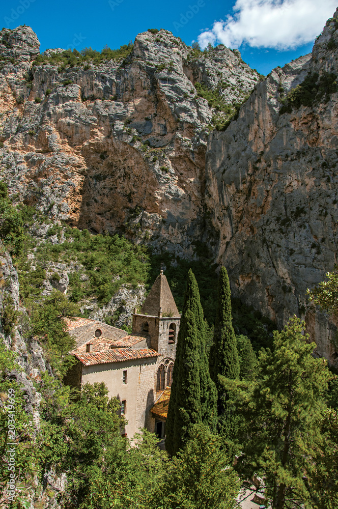 View of the church Notre-Dame de Beauvoir amid the cliffs, above the charming village of Moustiers-Sainte-Marie. In the Alpes-de-Haute-Provence department, Provence region, southeastern France View of the church Notre-Dame de Beauvoir amid the cliffs, above the charming village of Moustiers-Sainte-Marie. In the Alpes-de-Haute-Provence department, Provence region, southeastern France