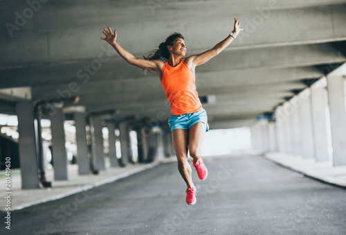Young female runner jumps on the street,expressing positive emotion.She made her goal of the day.Fitness and workout concept.