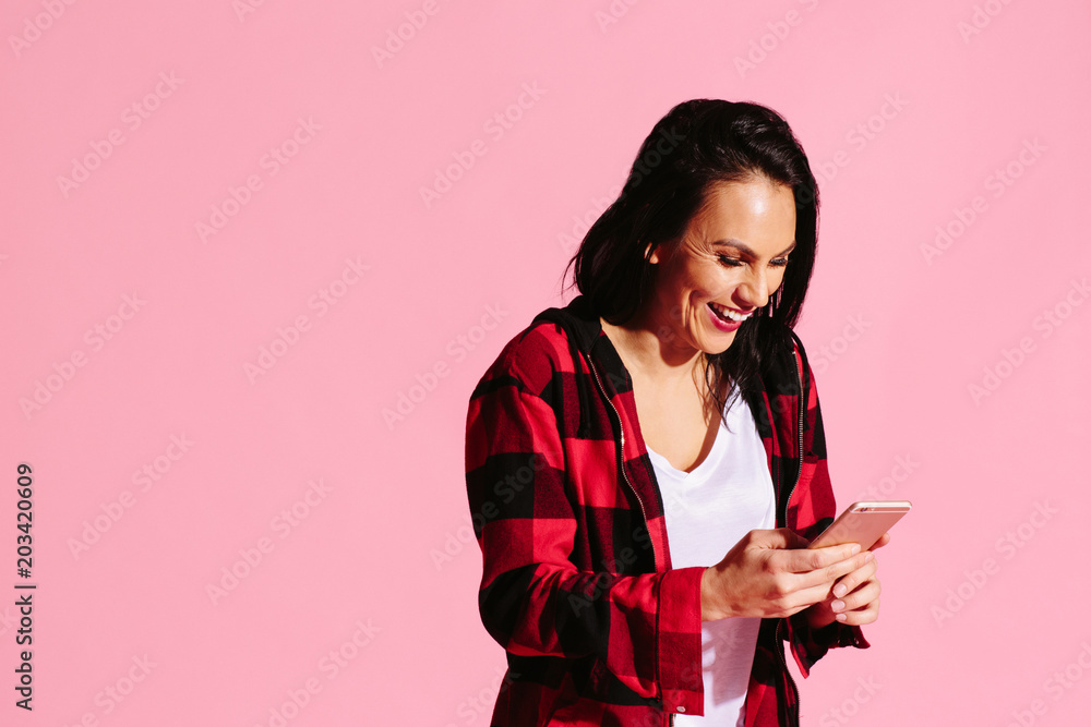 Young woman laughing while texting and holding cell phone, isolated on pink studio background Young woman laughing while texting and holding cell phone, isolated on pink studio background