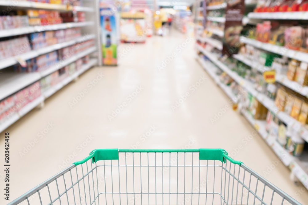 Supermarket aisle product shelves with empty green shopping cart defocused customer background