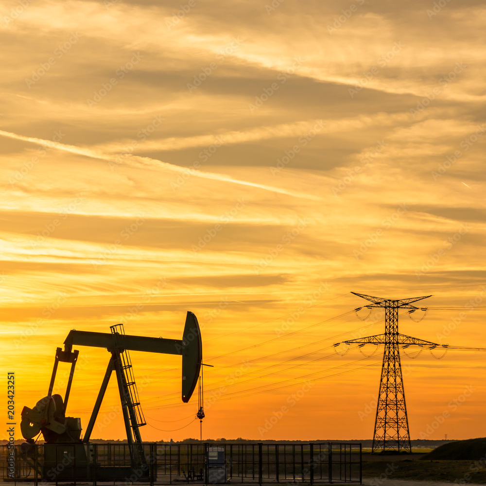 Pumpjack and transmission tower at sunset symbolizing energy transition