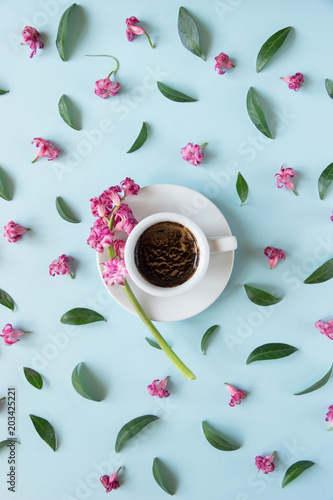 White cup with coffee on a blue background. Pattern of pink flowers and green leaves. Creative design. Concept. Flat lay