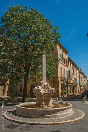 Street with buildings and fountain in sunny afternoon in Aix-en-Provence, a pleasant and lively town in the French countryside. In the Bouches-du-Rhone department, Provence region, southeastern France