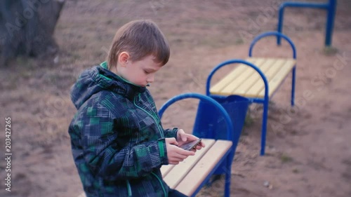 Boy plays a game on his mobile phone sitting in the Park on a bench. photo