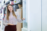 Positive salesgirl offering refrigerator in store