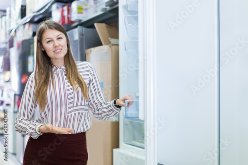 Positive salesgirl offering refrigerator in store