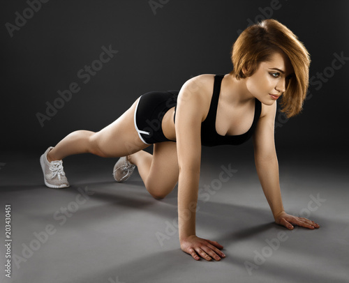 beautiful young woman doing push-ups on a dark background