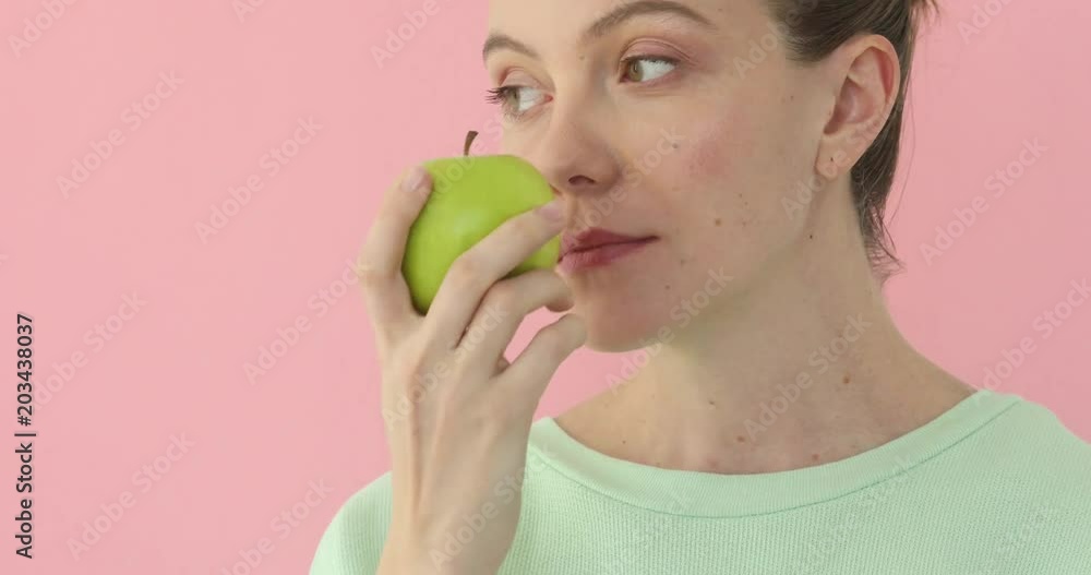 Woman sniffing an apple on a light background. Girl enjoying fresh fruit at pink background Woman sniffing an apple on a light background. Girl enjoying fresh fruit at pink background