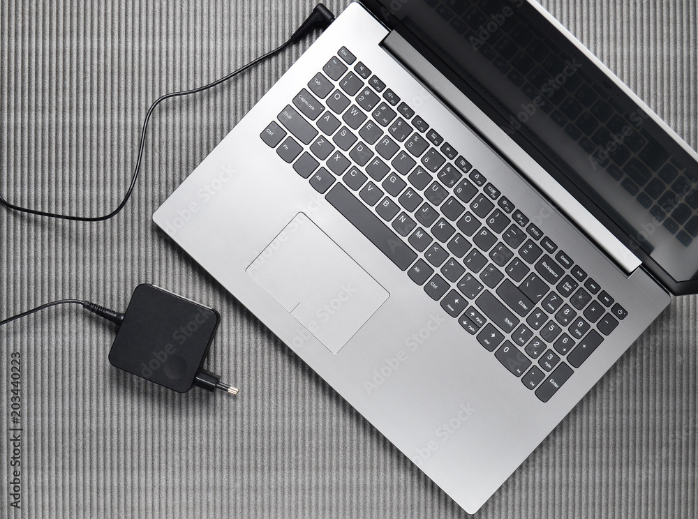 Φωτογραφία Laptop and charging for a laptop on a gray textured background, top view