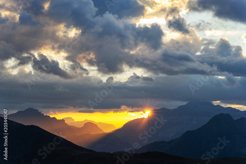 Red sunset in the mountains landscape with sunny beams. Dramatic scene of italian Dolomites with sun peaking behind a high mountains.