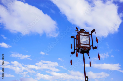 glass Chinese lantern with pendants on blue sky background with white clouds