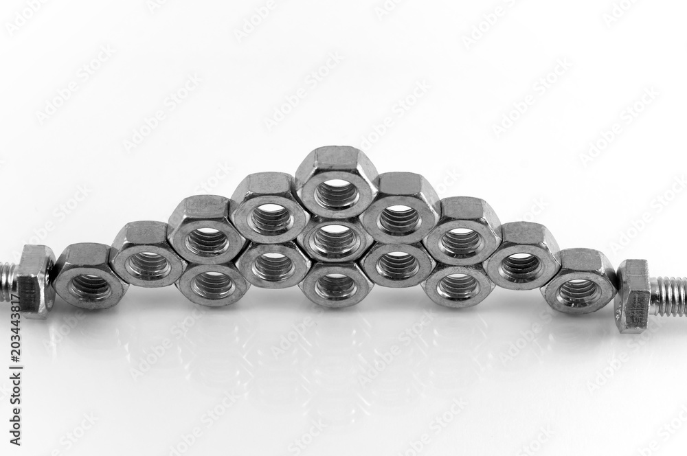 Steel hexahedral nuts stacked on top of each other in staggered order on a white background with reflection. Steel hexahedral nuts stacked on top of each other in staggered order on a white background with reflection.