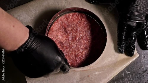 Cook makes meat medallions for burgers. Chef in black food gloves makes cutlet. Cutlets are leveled in steel ring in an even medallion. On top of pouring spices pepper and salt. Meat marbled beef lies photo