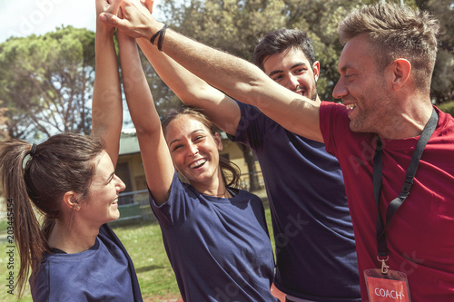 circle of happy sportive young athletes in sportswear raising hands