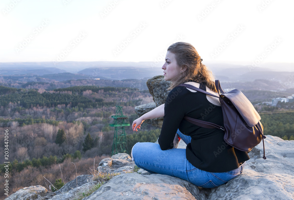 girl sitting on a rock over a mountain valley at sunset