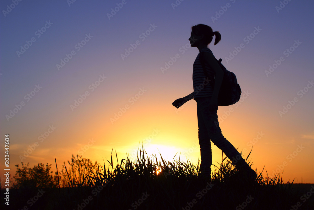 People, Teens, Hiking and Travel Concept. Silhouette Of A Young Girl On A Mountain Top.Young Girl With Backpack Enjoying Sunset.Tourist Traveler At Sunset.
