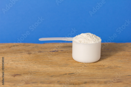 Whey Protein. Close up of scoop filled with vanilla flavour powder over wood table. Color background: blue.