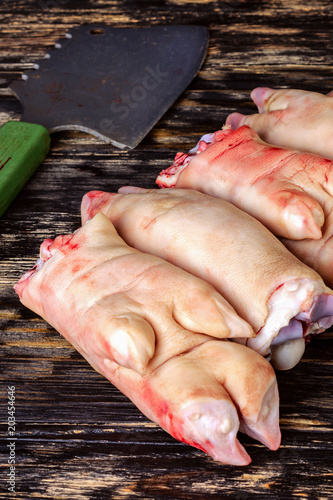 Raw and freesh pork feet or legs,over dark wooden board. They are stacked pile. With a cutting ax. Food meat shot. Vertical.
