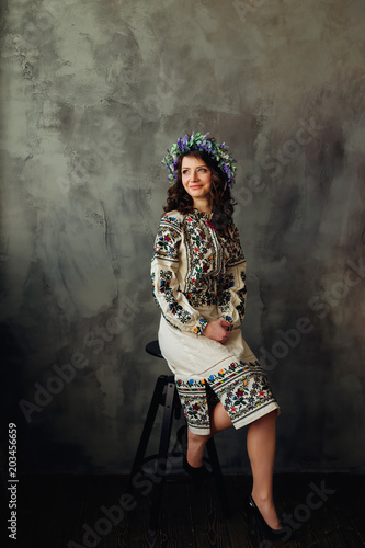 beautiful woman in national clothes sitting on a chair and with a chic flower wreath on her head