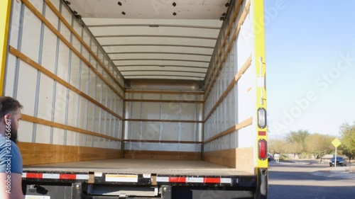 Wide shot of a man pushing in a metal ramp on a moving truck in 4k. The young mover puts the loading ramp away into the back of the rental van. Shot represents relocating for work and a fresh start.