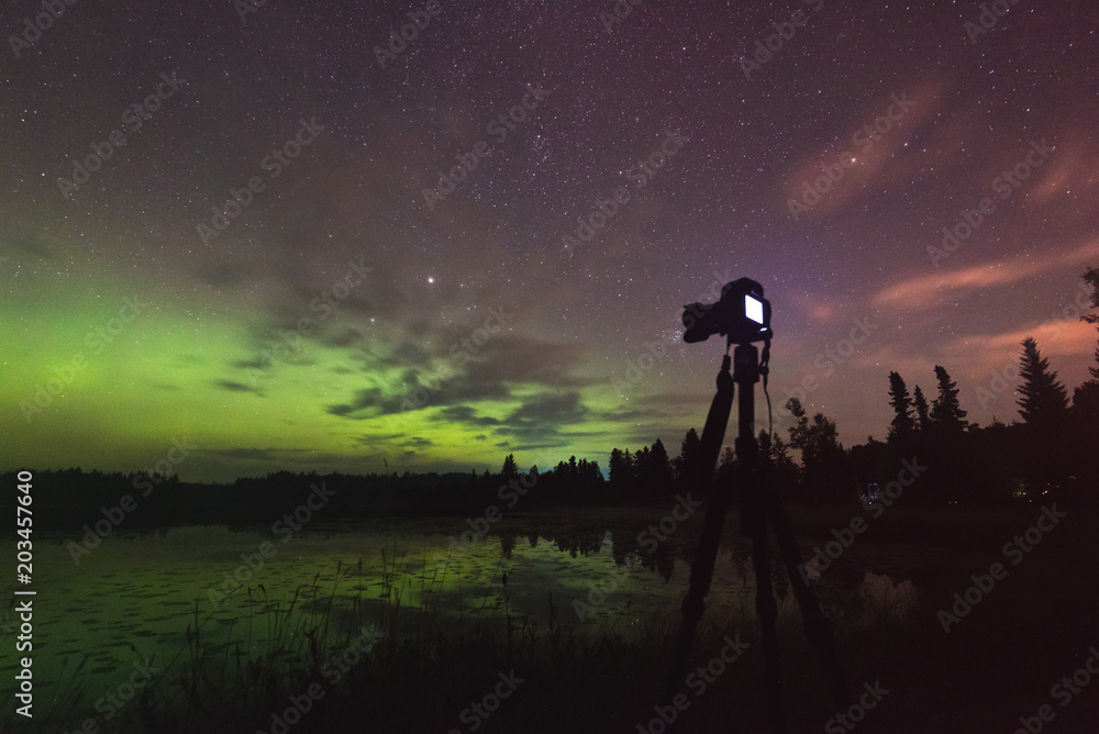 Aurora reflecting of a lake, city lights lighting up clouds - Camera in forground