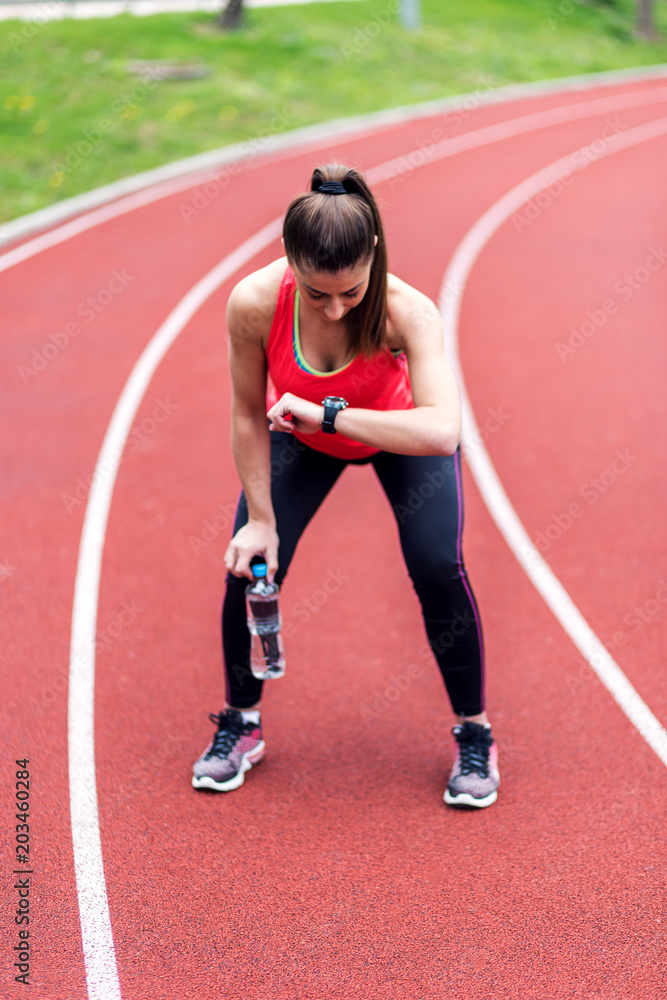 Obraz premium Female runner looking at smartwatch after running on racetrack