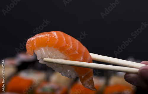 Chopsticks holding salmon sushi on black background
