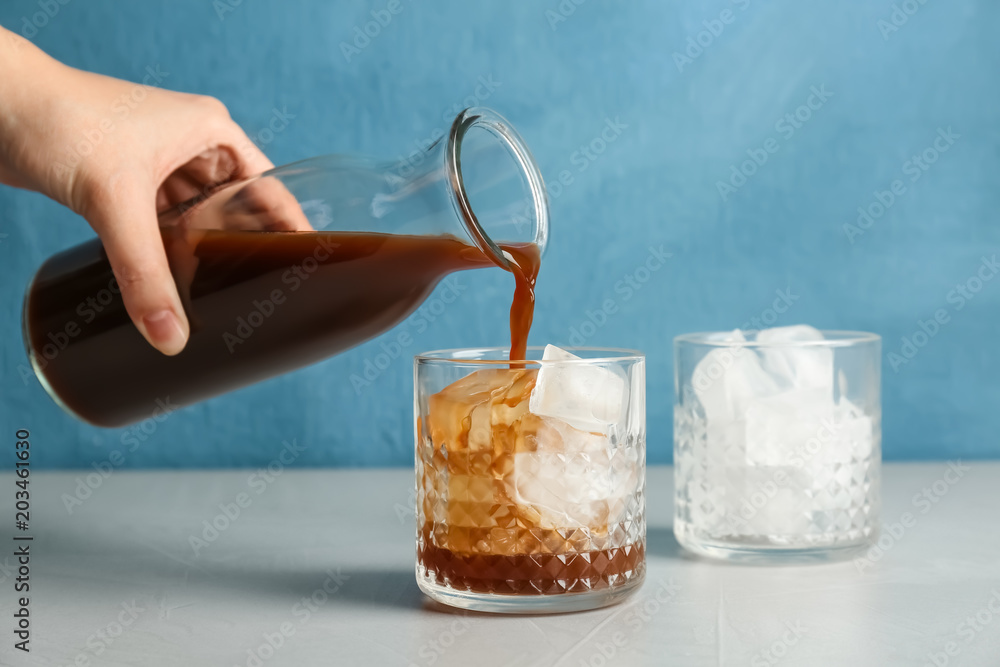 Woman pouring cold brew coffee into glass on table - obrazy, fototapety, plakaty 