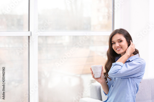Beautiful young woman with cup of coffee near window © New Africa
