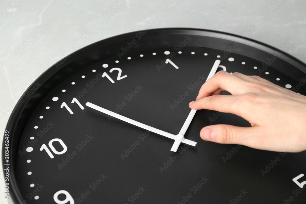 Woman changing time on big black clock, closeup Woman changing time on big black clock, closeup
