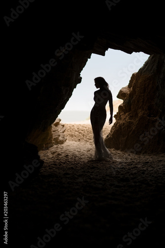 Beautiful and sexy woman body silhouette in long dress in a cave
