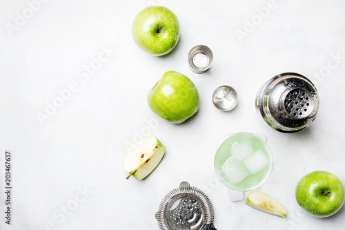 Alcoholic cocktail with green apple and dry vermouth, syrup, lemon juice and ice cubes. Bar tools, gray stone background, top view